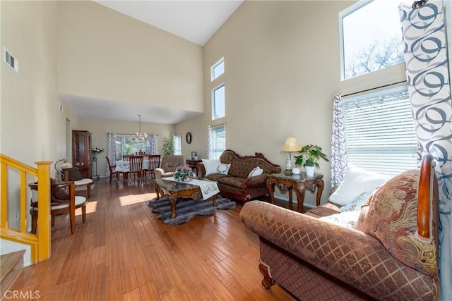 living area featuring an inviting chandelier, a high ceiling, wood-type flooring, and visible vents
