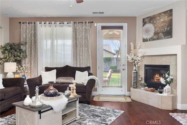 living area with wood-type flooring, visible vents, a tiled fireplace, and a wealth of natural light