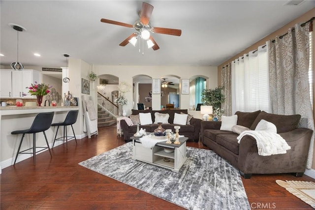 living room with stairs, a ceiling fan, arched walkways, and dark wood-style flooring