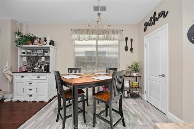 dining area featuring visible vents, light wood-style flooring, baseboards, and a notable chandelier