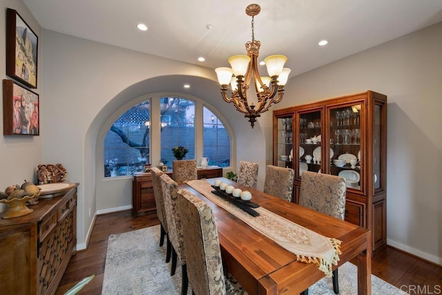 dining space with an inviting chandelier, arched walkways, dark wood finished floors, recessed lighting, and baseboards