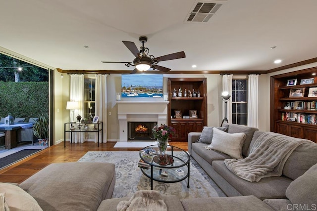 living room featuring visible vents, ornamental molding, wood finished floors, a lit fireplace, and a ceiling fan