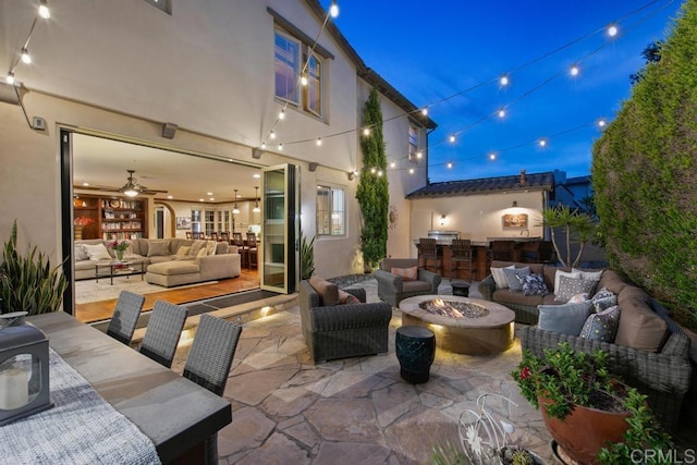 patio at night with an outdoor living space with a fire pit and an outdoor kitchen