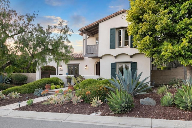 view of front of home featuring stucco siding, fence, a balcony, and a tile roof