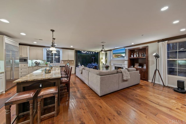 living room featuring recessed lighting, wood-type flooring, a ceiling fan, and a warm lit fireplace