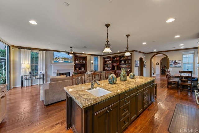 kitchen with a warm lit fireplace, a sink, arched walkways, recessed lighting, and ornamental molding