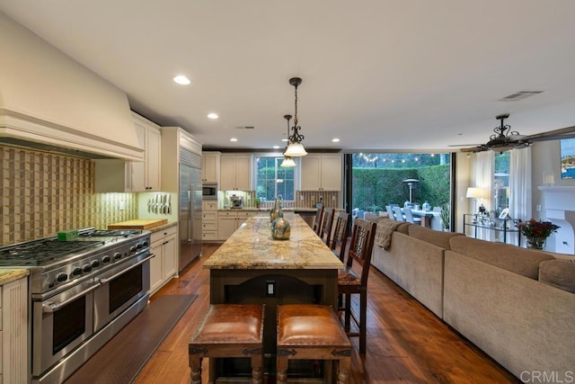 kitchen with visible vents, built in appliances, custom exhaust hood, open floor plan, and a breakfast bar area