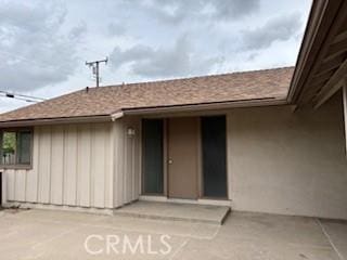 doorway to property with stucco siding, roof with shingles, and a patio area