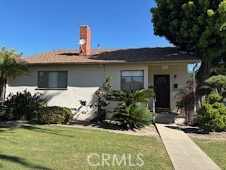 single story home with a chimney, stucco siding, and a front yard