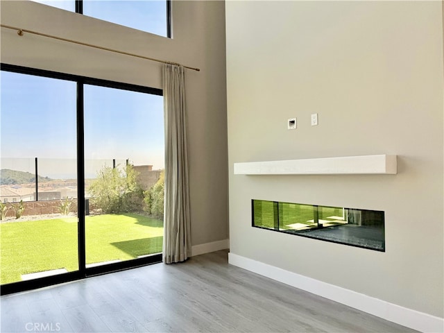 spare room featuring baseboards, a high ceiling, a glass covered fireplace, and wood finished floors