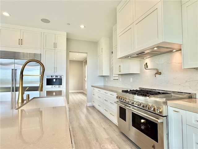 kitchen with white cabinets, range with two ovens, baseboards, decorative backsplash, and light wood-type flooring