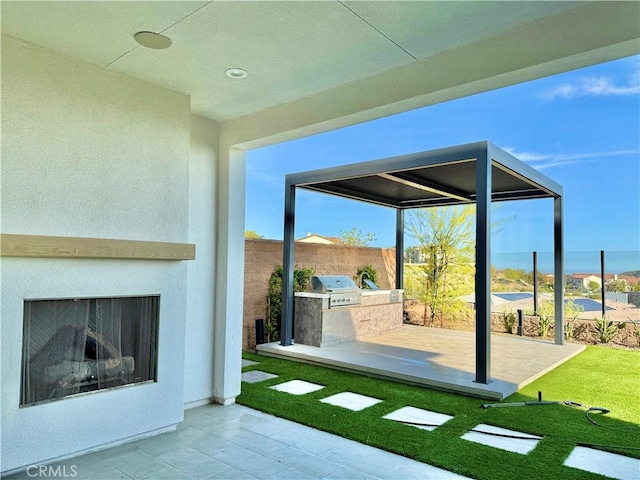 view of patio featuring an outdoor kitchen, fence, an outdoor fireplace, and area for grilling