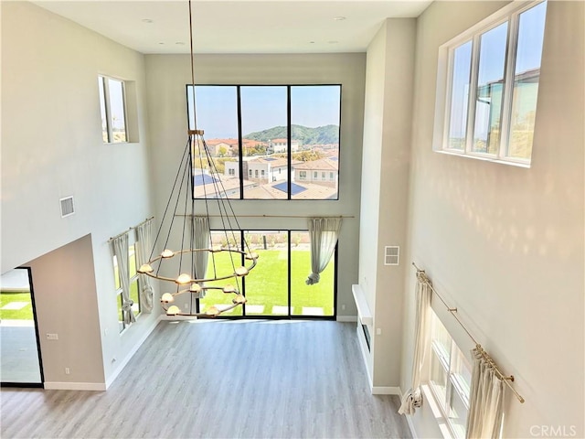 interior space with visible vents, a towering ceiling, wood finished floors, and a healthy amount of sunlight
