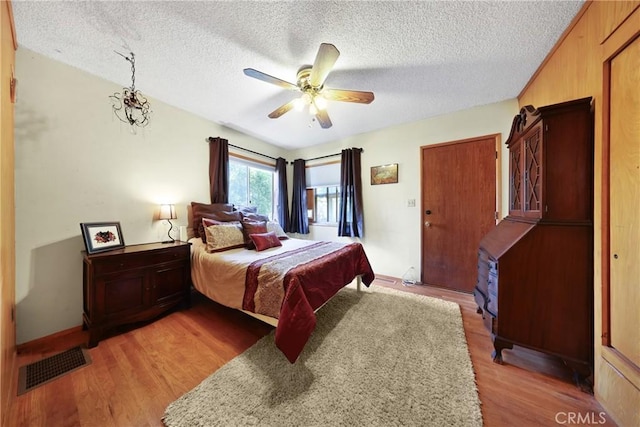 bedroom with ceiling fan, light wood-type flooring, a textured ceiling, and visible vents