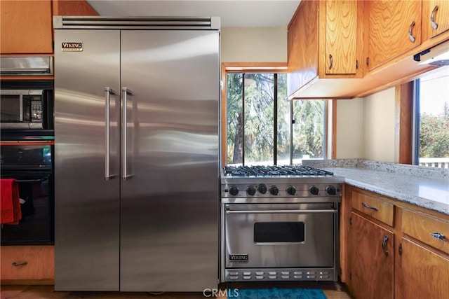 kitchen with light stone counters, premium appliances, and brown cabinetry