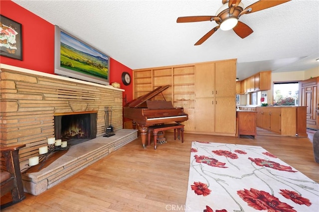 interior space featuring a ceiling fan, a textured ceiling, a stone fireplace, vaulted ceiling, and light wood-style floors