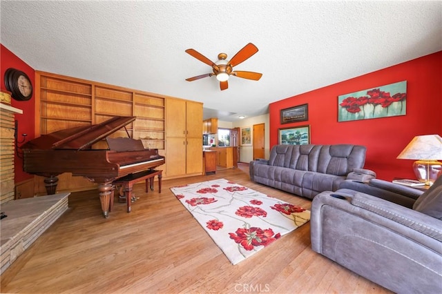 living room featuring light wood-style floors, ceiling fan, and a textured ceiling