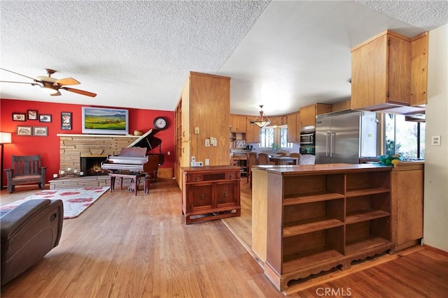 kitchen with ceiling fan, a textured ceiling, light wood-type flooring, open floor plan, and built in appliances