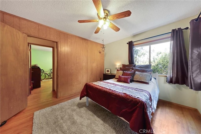 bedroom with light wood-style floors, ceiling fan, wooden walls, and a textured ceiling