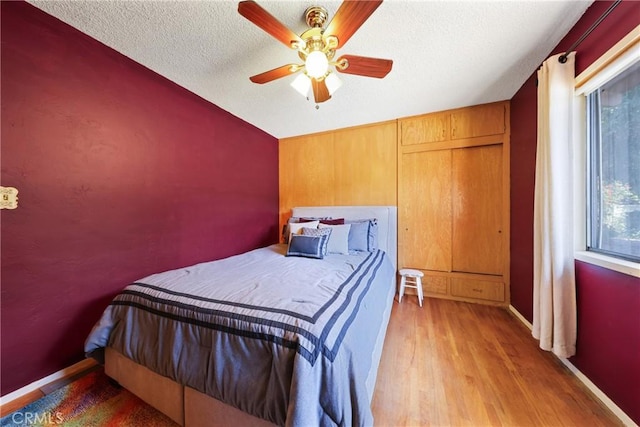bedroom with a textured ceiling, ceiling fan, and light wood-style flooring