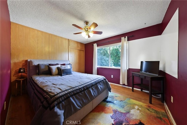 bedroom with wooden walls, ceiling fan, a textured ceiling, wood finished floors, and a closet