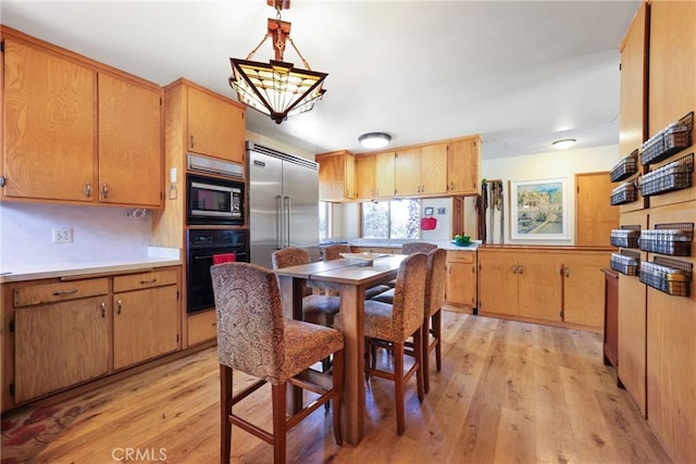 kitchen with pendant lighting, built in appliances, light countertops, a chandelier, and light wood-style flooring