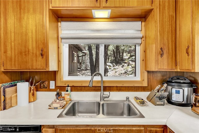 kitchen with light countertops, brown cabinetry, a sink, and dishwasher