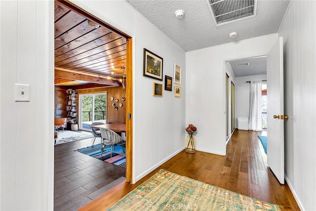 corridor with wooden walls, wood-type flooring, a textured ceiling, baseboards, and visible vents