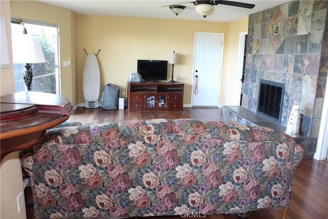 living room featuring a tiled fireplace, a ceiling fan, baseboards, and wood finished floors