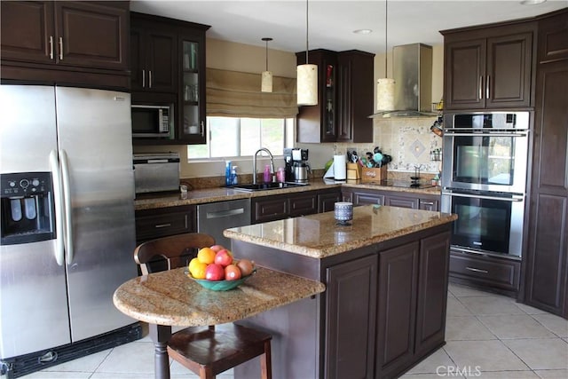 kitchen featuring glass insert cabinets, wall chimney range hood, a sink, light tile patterned floors, and stainless steel appliances