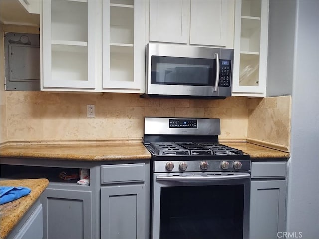 kitchen featuring glass insert cabinets, light countertops, backsplash, and stainless steel appliances