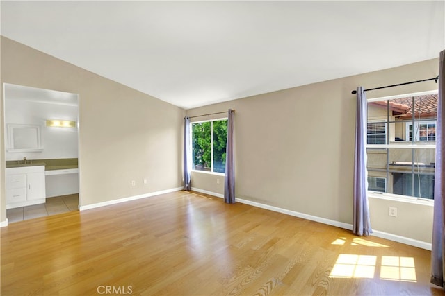 spare room with light wood-style floors, a sink, baseboards, and vaulted ceiling