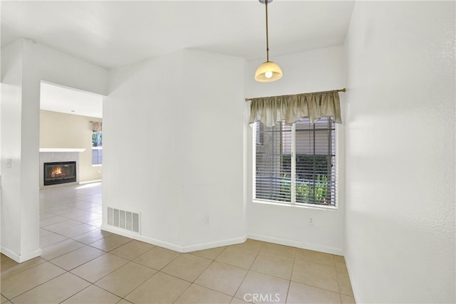 tiled empty room featuring baseboards, visible vents, and a tiled fireplace