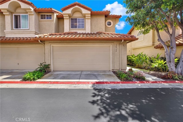 view of front of house featuring an attached garage, driveway, a tile roof, and stucco siding