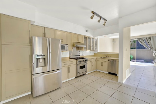 kitchen with a sink, appliances with stainless steel finishes, under cabinet range hood, and light tile patterned flooring