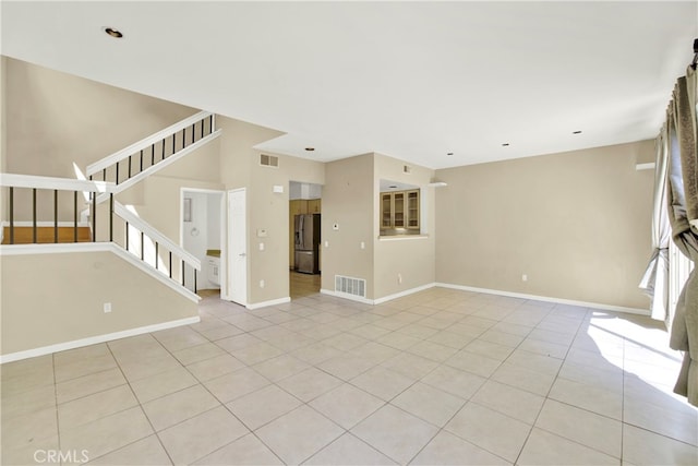 unfurnished living room with baseboards, visible vents, light tile patterned floors, and stairway