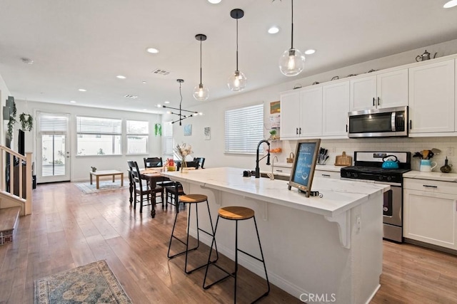 kitchen featuring a center island with sink, white cabinets, a breakfast bar area, and stainless steel appliances