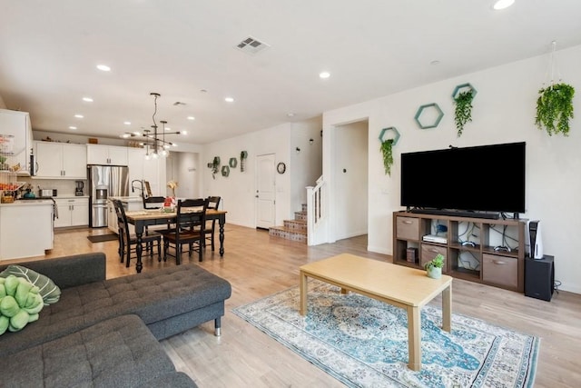 living area with visible vents, light wood-type flooring, stairway, an inviting chandelier, and recessed lighting