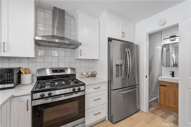 16266 Sigman St, Hacienda Heights, CA 91745 - kitchen featuring wall chimney range hood, appliances with stainless steel finishes, white cabinetry, a sink, and light wood-style flooring