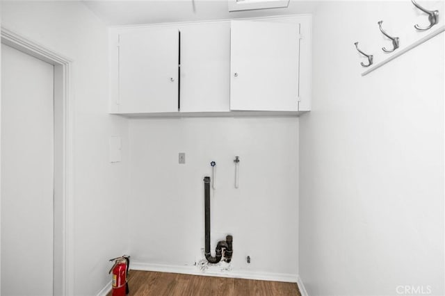 clothes washing area with cabinet space, baseboards, and wood finished floors