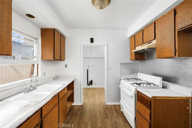 kitchen with white gas range, light countertops, a sink, dark wood-style floors, and under cabinet range hood