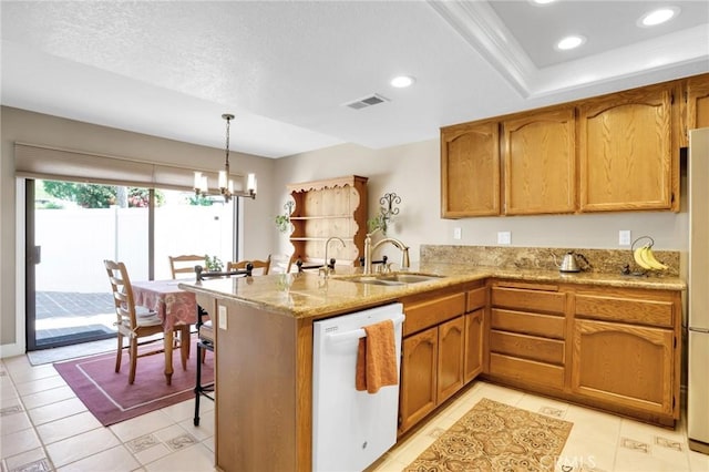 kitchen featuring visible vents, dishwasher, a sink, a peninsula, and a chandelier