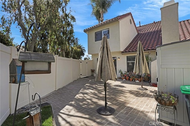 rear view of property featuring fence, a chimney, a tile roof, and a patio area