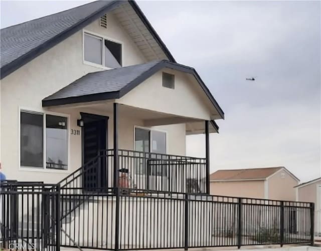 back of house featuring a shingled roof, stucco siding, and fence private yard