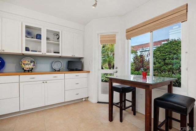 kitchen with wood counters, light tile patterned flooring, white cabinets, and glass insert cabinets