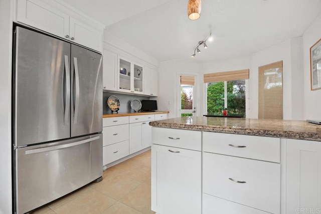 kitchen featuring freestanding refrigerator, light stone countertops, glass insert cabinets, white cabinetry, and light tile patterned floors