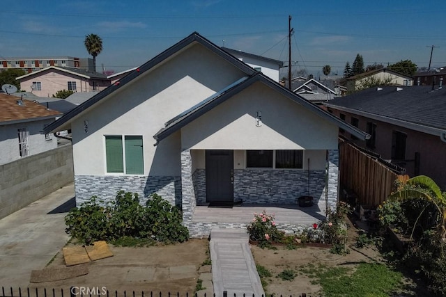 bungalow featuring fence, stucco siding, and stone siding