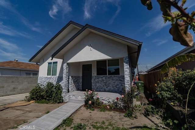 bungalow-style home with fence, stucco siding, and stone siding