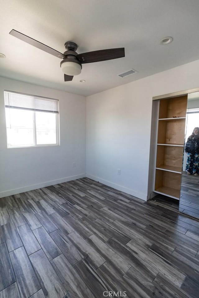 empty room with visible vents, dark wood finished floors, ceiling fan, and baseboards