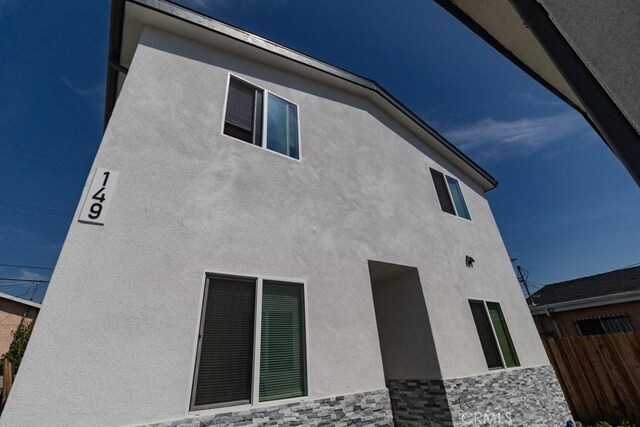 view of home's exterior with stucco siding, fence, and stone siding